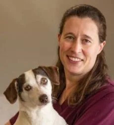 female veterinarian with medium length brown hair holding small white and brown dog
